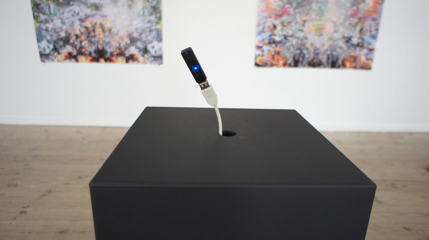 configuration no. 7 — the black pedestal with a USB stick plugged into its port, collage prints on the wall behind