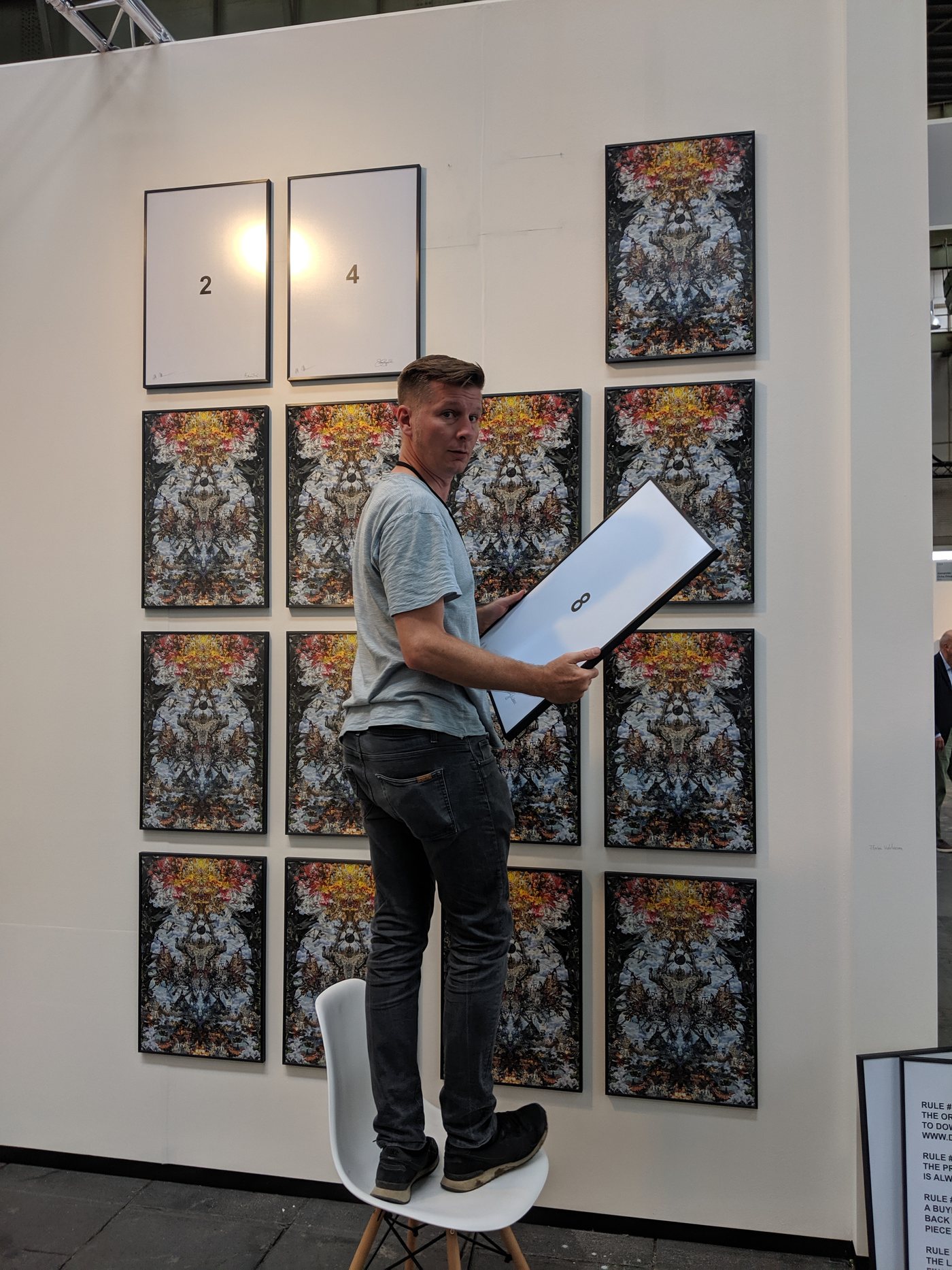 art berlin 2019 — the artist on a chair, swapping print no. 8 for its number sheet; the wall still almost full of dystopia_deathstar prints