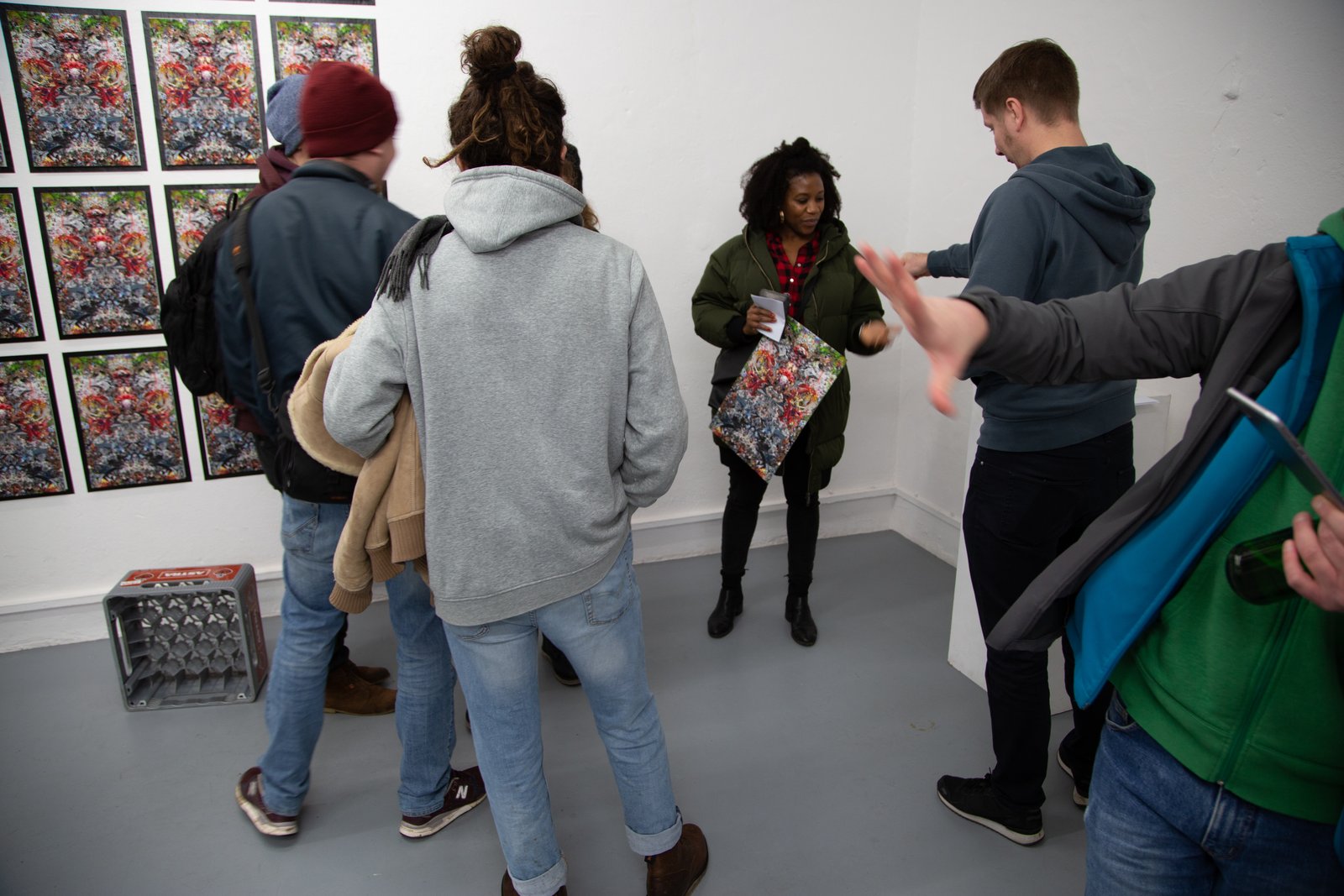 Selling the new project — visitors at the wall of identical prints, a sold piece changing hands during the happening